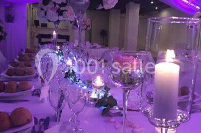 Décor champêtre avec fauteuils, tapis, grande horloge et lanternes sous un arbre, ambiance vintage en extérieur.