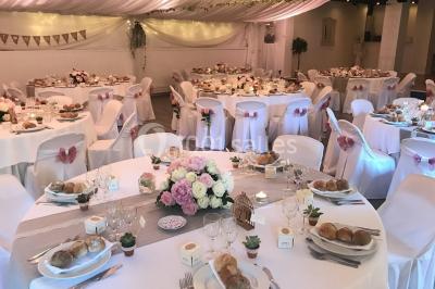 Décor champêtre avec fauteuils, tapis, grande horloge et lanternes sous un arbre, ambiance vintage en extérieur.