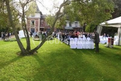 Décor champêtre avec fauteuils, tapis, grande horloge et lanternes sous un arbre, ambiance vintage en extérieur.