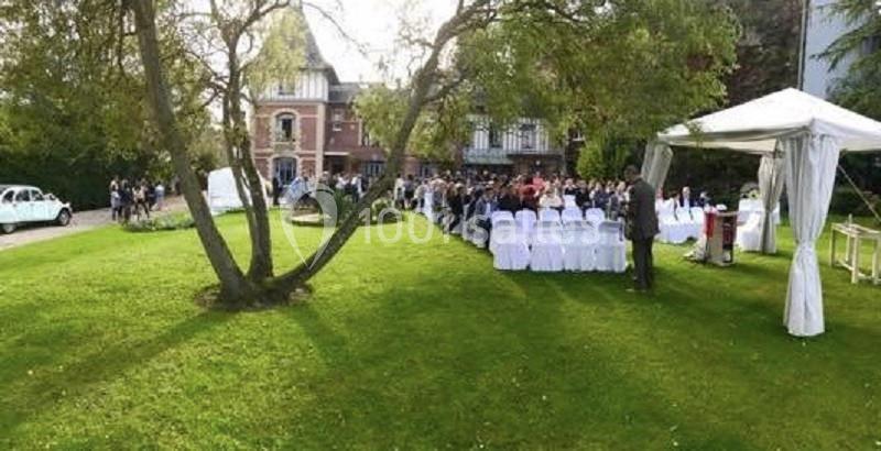 Cérémonie en plein air avec des invités assis sous une tente blanche, dans un jardin devant un bâtiment ancien.