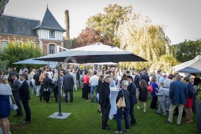 Décor champêtre avec fauteuils, tapis, grande horloge et lanternes sous un arbre, ambiance vintage en extérieur.