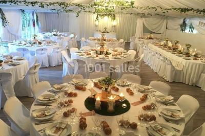 Décor champêtre avec fauteuils, tapis, grande horloge et lanternes sous un arbre, ambiance vintage en extérieur.