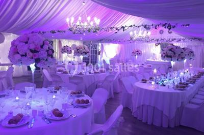 Décor champêtre avec fauteuils, tapis, grande horloge et lanternes sous un arbre, ambiance vintage en extérieur.