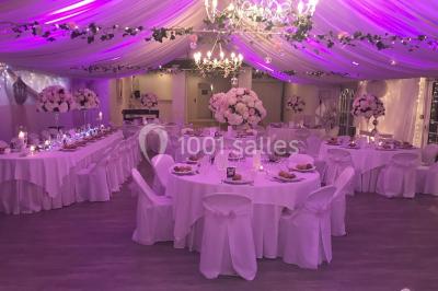 Décor champêtre avec fauteuils, tapis, grande horloge et lanternes sous un arbre, ambiance vintage en extérieur.