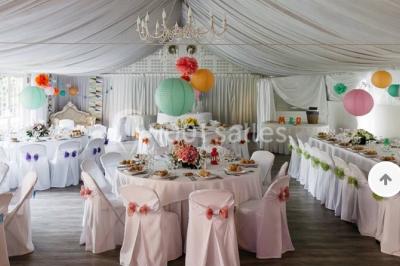 Décor champêtre avec fauteuils, tapis, grande horloge et lanternes sous un arbre, ambiance vintage en extérieur.