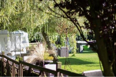 Décor champêtre avec fauteuils, tapis, grande horloge et lanternes sous un arbre, ambiance vintage en extérieur.