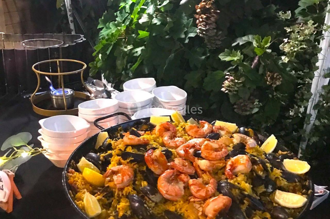 Grande poêle de paella garnie de crevettes, moules et quartiers de citron, présentée sur une table en extérieur.