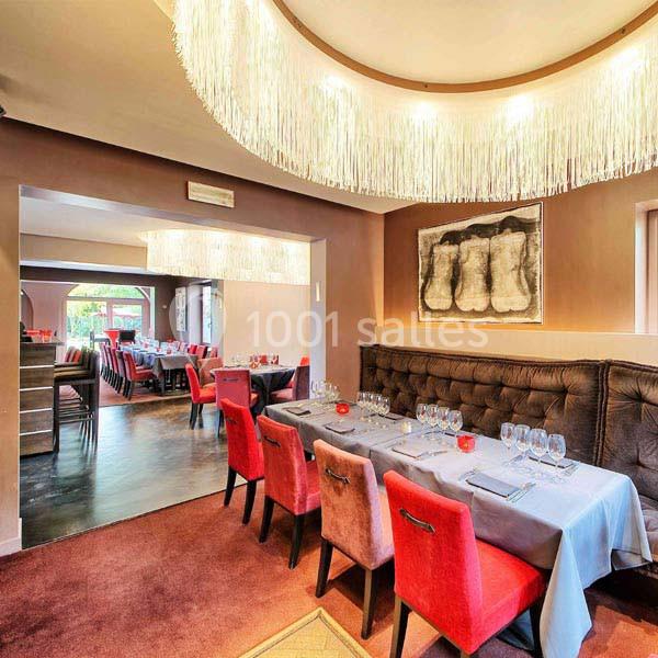 Salle de restaurant élégante avec tables dressées, chaises rouges et lustres modernes suspendus.