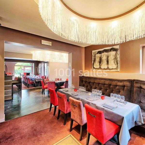 Salle de restaurant élégante avec tables dressées, chaises rouges et éclairage moderne suspendu.