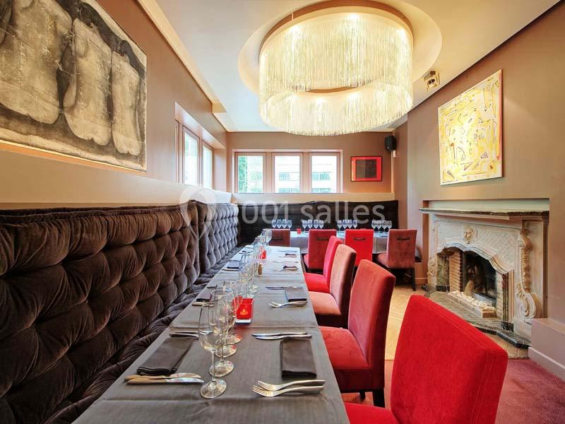Salle de restaurant élégante avec banquettes en velours, chaises rouges, cheminée et lustre moderne.