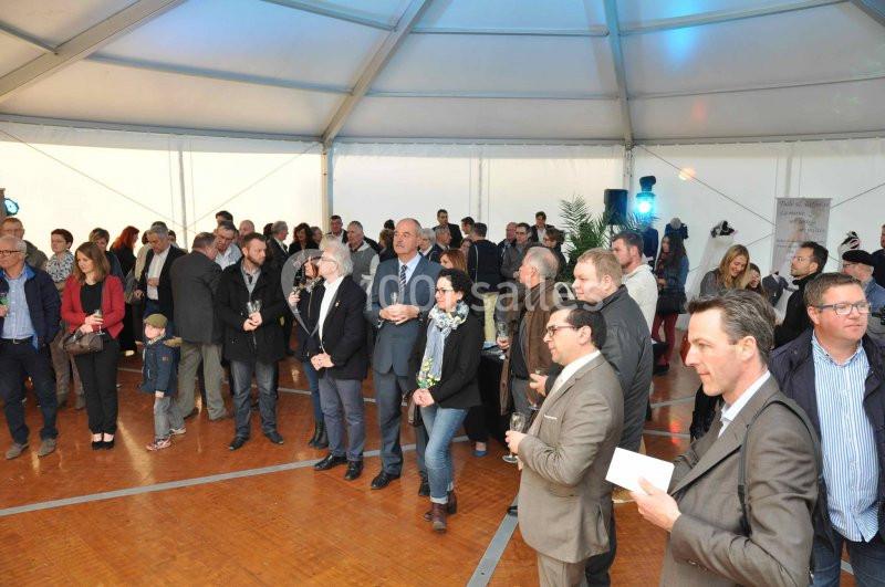 Groupe de personnes rassemblées dans une grande tente pour un événement, certaines debout et d'autres discutant.