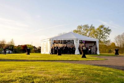 Tente blanche installée sur une pelouse, accueillant un événement avec des invités debout autour de tables hautes.