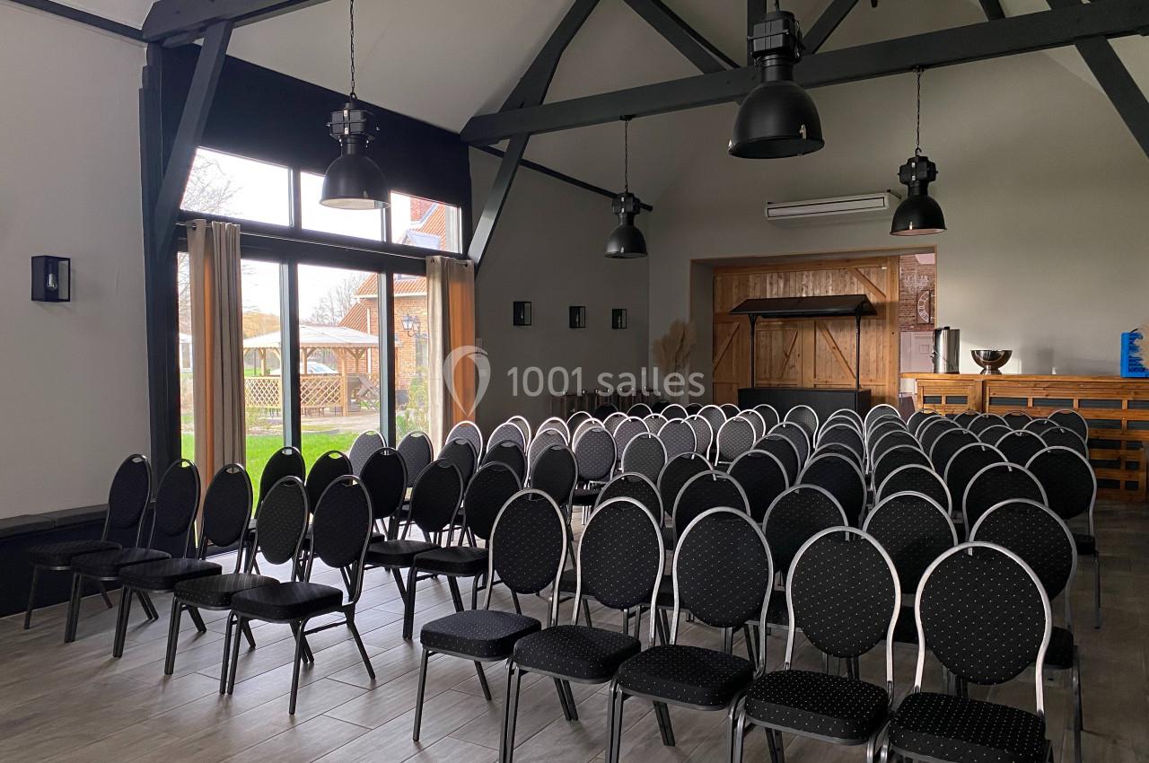 Salle de réunion lumineuse avec des rangées de chaises noires alignées face à une grande baie vitrée.