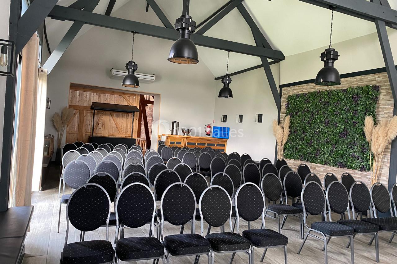 Salle de réunion avec des rangées de chaises noires, poutres apparentes et mur végétal décoratif.