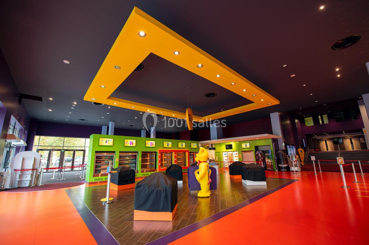 Hall coloré avec un plafond jaune géométrique, des comptoirs couverts et des étagères vertes dans un espace lumineux.