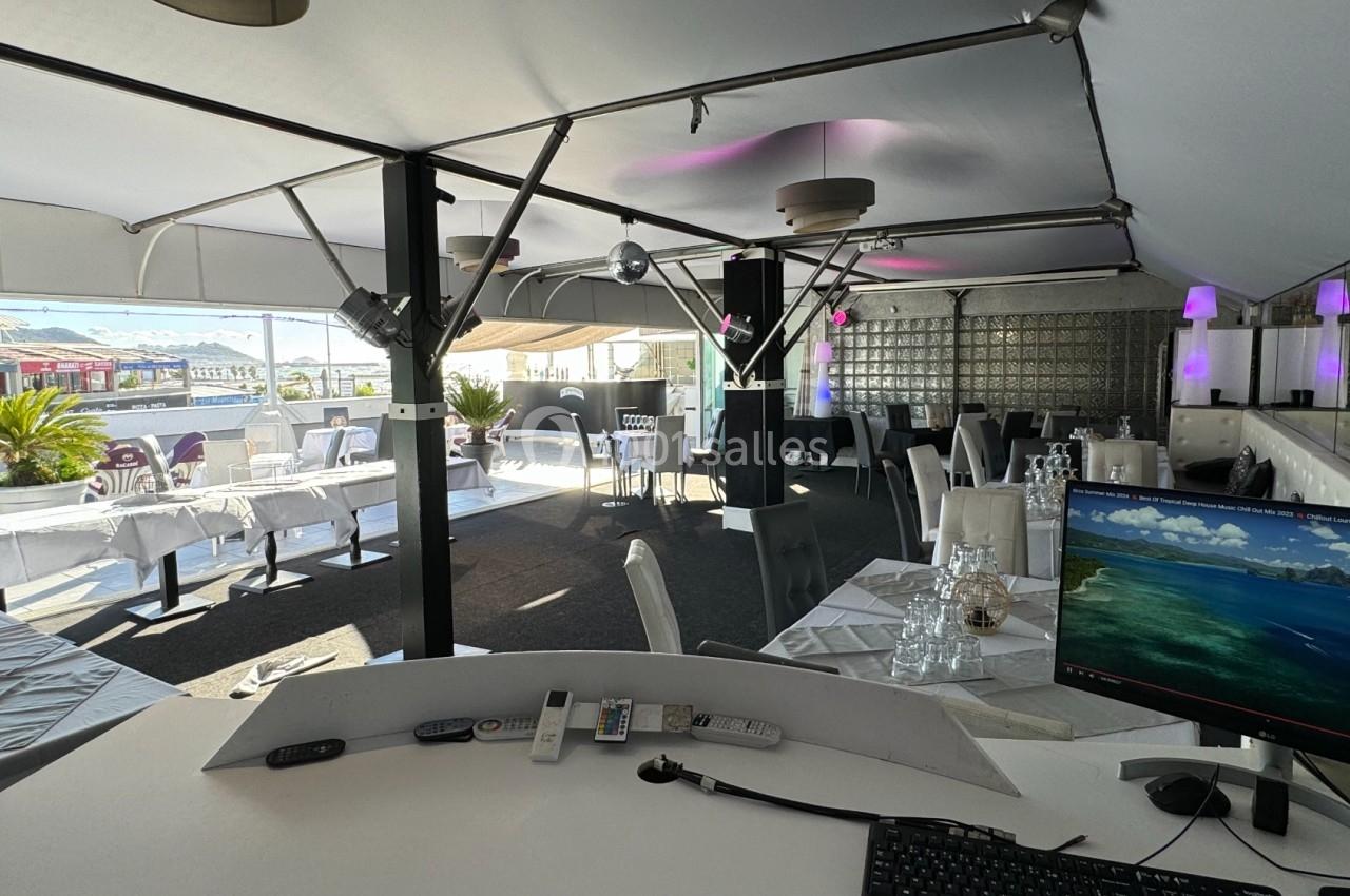 Salle de restaurant lumineuse avec tables dressées, vue sur une terrasse extérieure et un poste informatique au premier plan.