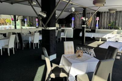 Salle de restaurant lumineuse avec tables dressées, chaises noires et blanches, et terrasse extérieure avec vue sur des…