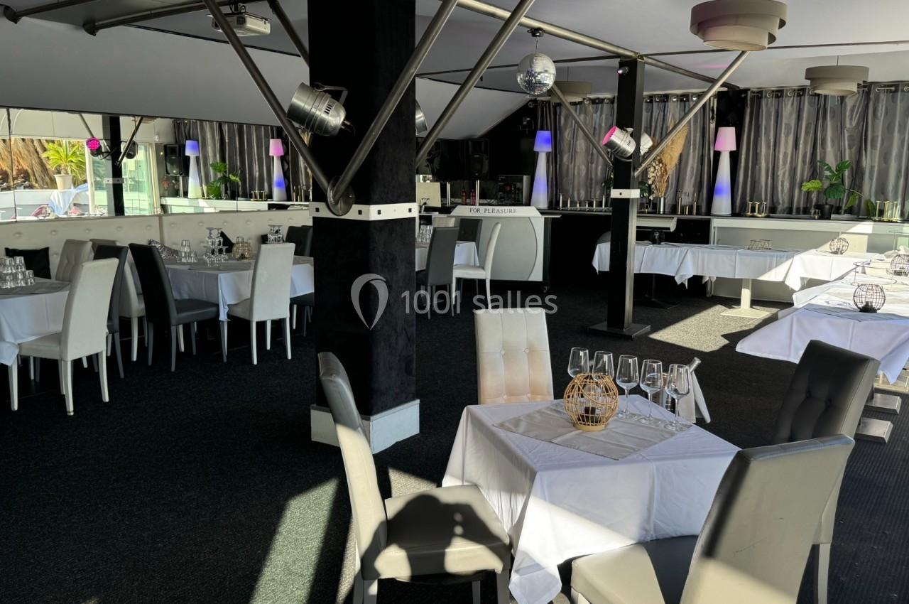 Salle de restaurant lumineuse avec tables dressées, chaises modernes et grandes baies vitrées laissant entrer la lumière.