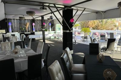 Salle de restaurant lumineuse avec tables dressées, chaises noires et blanches, et terrasse extérieure avec vue sur des…