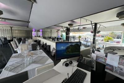 Salle de restaurant lumineuse avec tables dressées, chaises noires et blanches, et terrasse extérieure avec vue sur des…