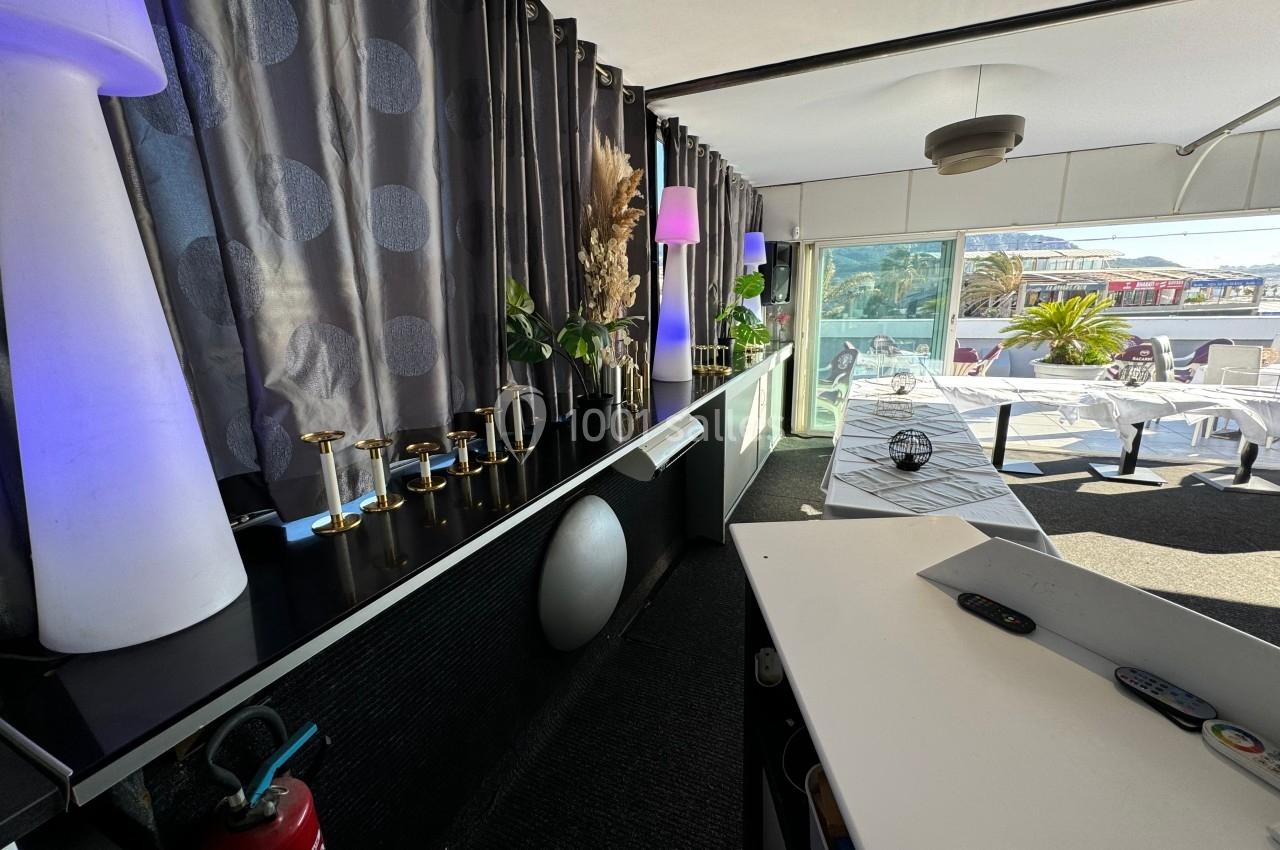 Intérieur d'un restaurant avec une table dressée près d'une baie vitrée donnant sur une terrasse ensoleillée.