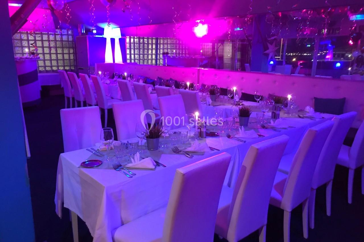 Salle de réception décorée avec des tables dressées, éclairage coloré et ambiance festive.