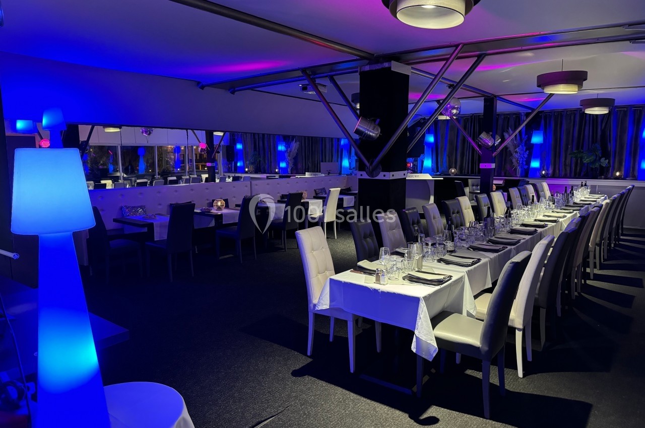 Salle de restaurant moderne avec tables dressées, éclairage tamisé et ambiance lumineuse bleutée.