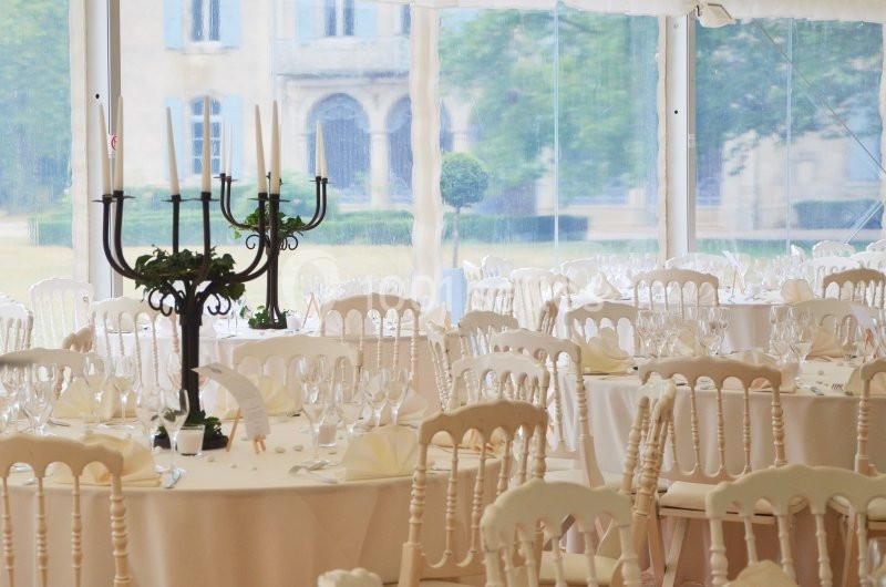 Salle de réception décorée avec des tables rondes, nappes blanches, chandeliers noirs et vue sur un jardin.