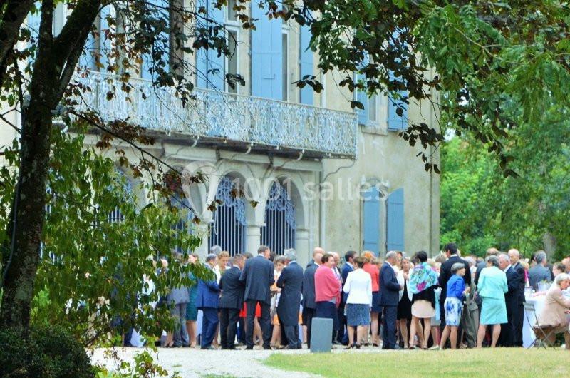 Groupe de personnes rassemblées devant une grande maison ancienne avec des volets bleus, entourée de verdure.