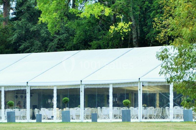 Grande tente blanche avec des parois transparentes, aménagée avec des tables et des chaises, entourée de verdure.