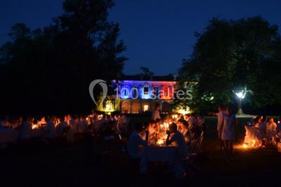 Des personnes en tenue blanche brandissent des cierges magiques lors d'un dîner en plein air devant un bâtiment éclairé.