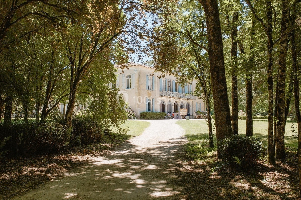 Allée ombragée menant à une grande maison de campagne entourée d'arbres et de verdure.