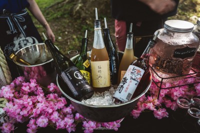 Vue d'une tente éclairée de nuit dans un jardin, entourée d'arbres sous un ciel crépusculaire.