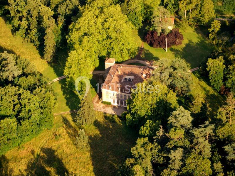 Vue aérienne d'une maison ancienne entourée d'arbres et de pelouses dans un paysage verdoyant.