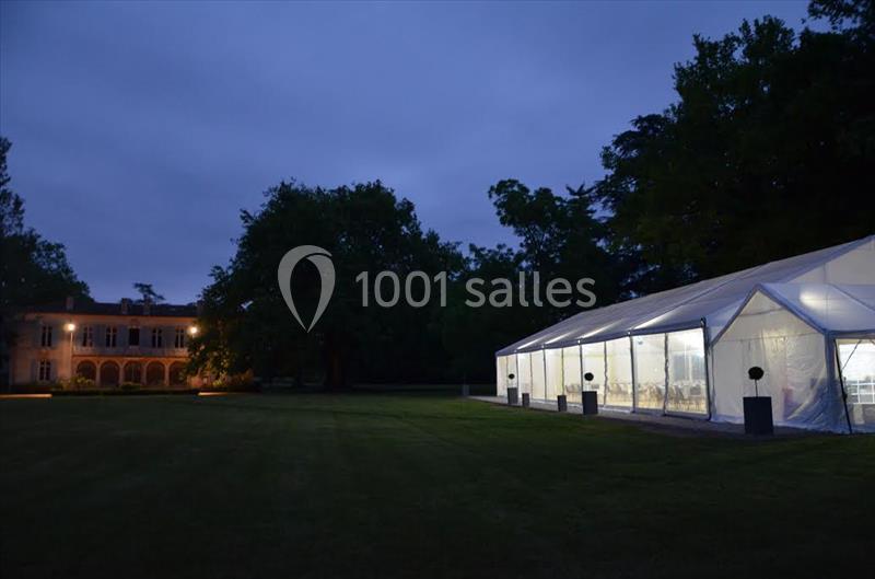 Une tente éclairée installée sur une pelouse au crépuscule, avec un bâtiment en arrière-plan.