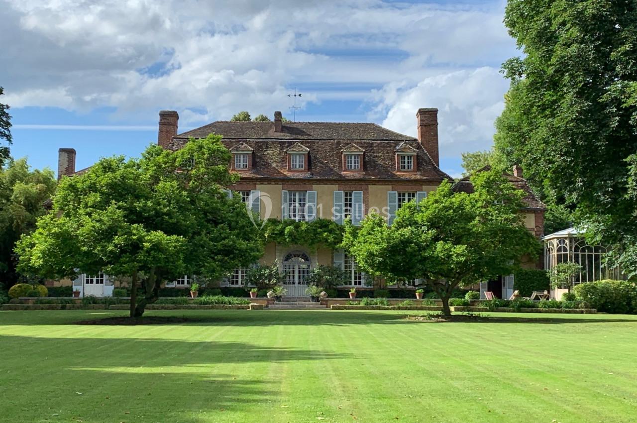 Façade d'un grand manoir en pierre avec toit en tuiles, entouré d'arbres et d'une pelouse bien entretenue.