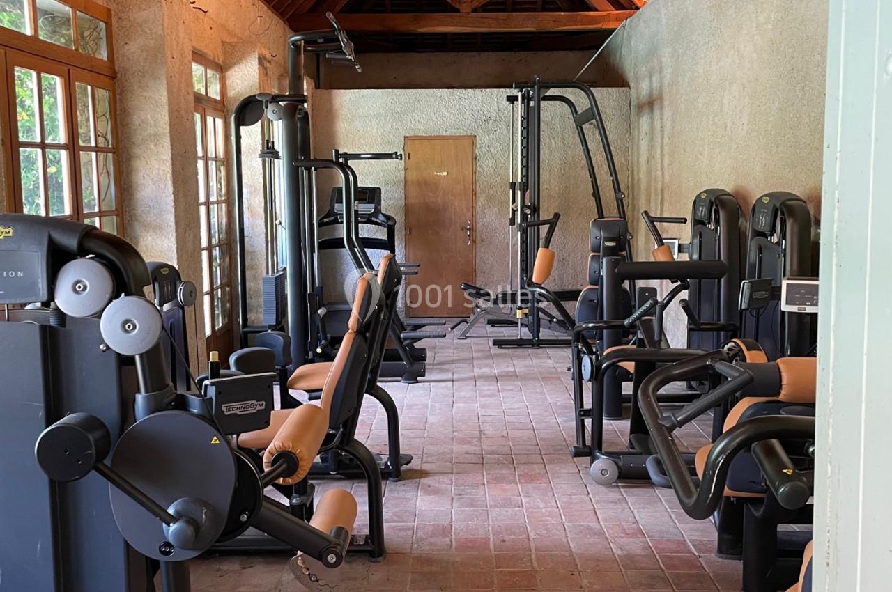 Salle de sport avec équipements de musculation modernes, sol en briques et plafond en bois.
