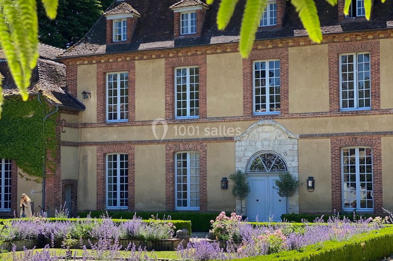 Façade d'une maison de campagne en pierre entourée de lavande et de haies, sous des branches de fougère.