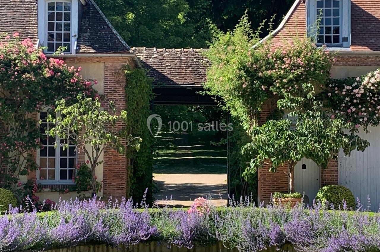 Cour avec bassin central, fontaine, fleurs colorées et deux bâtiments en briques entourés de verdure.