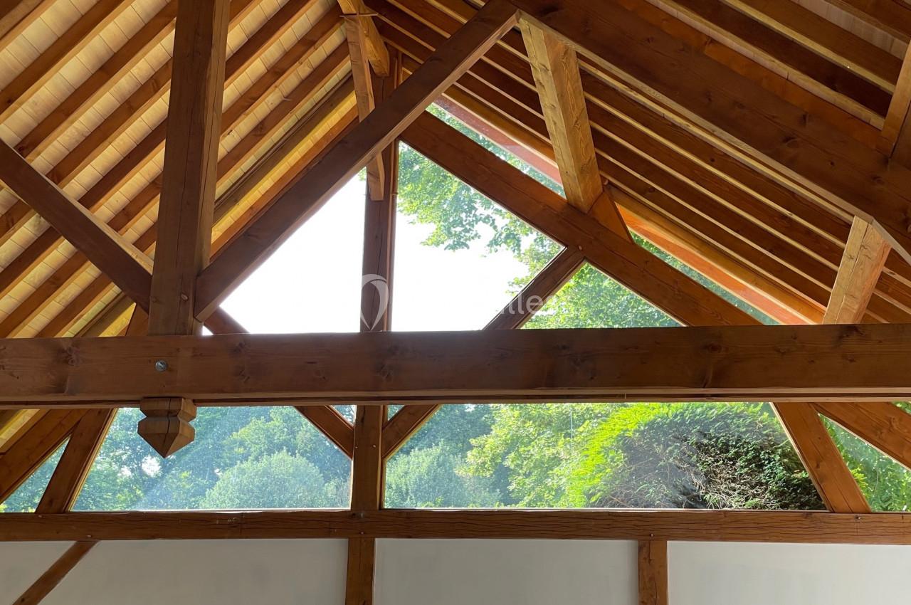 Charpente en bois apparente avec vue sur un extérieur verdoyant à travers une grande ouverture triangulaire.
