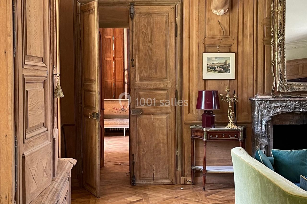 Intérieur d'une pièce avec boiseries murales, parquet, cheminée, canapé vert et tête d'antilope accrochée au mur.