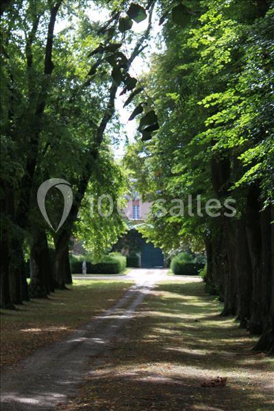 Allée bordée d'arbres menant à une maison en briques avec une porte verte, sous un éclairage naturel.