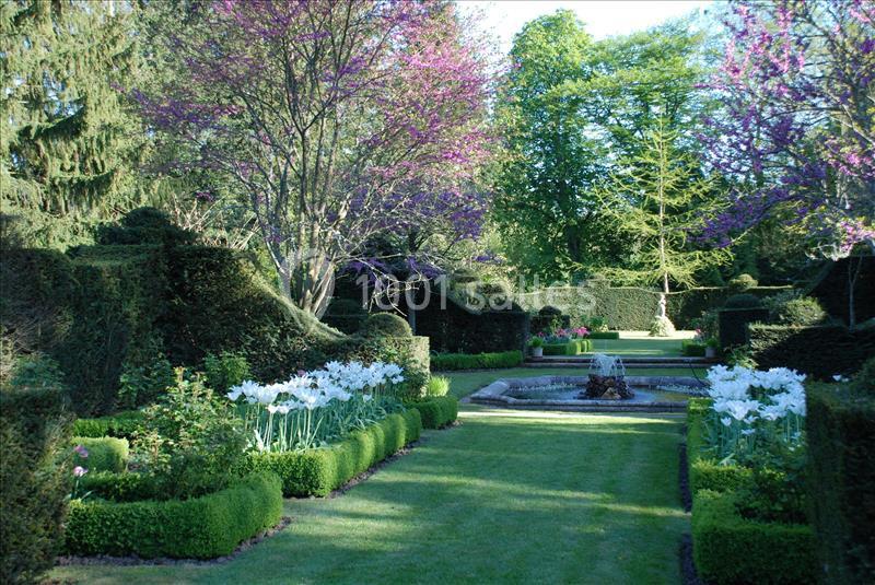 Jardin aménagé avec haies taillées, parterres fleuris, pelouse entretenue et fontaine centrale entourée de verdure.