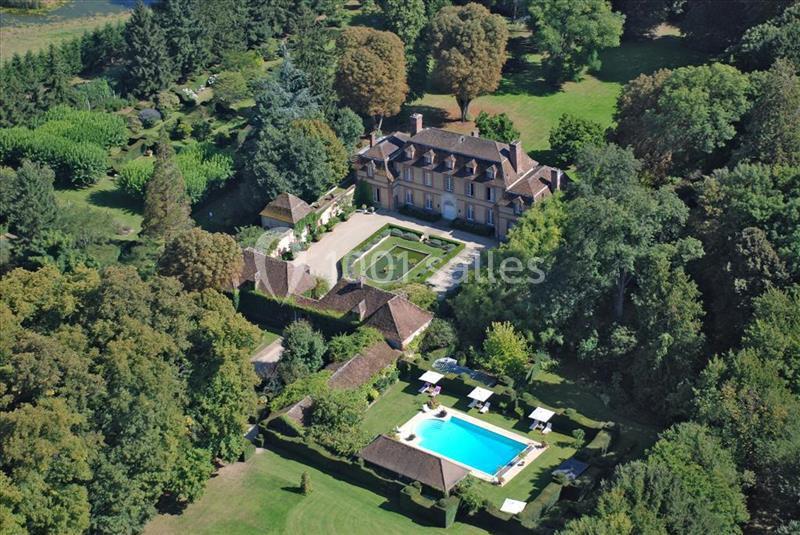 Vue aérienne d'un domaine avec un manoir, des jardins aménagés, une piscine et des espaces verts entourés d'arbres.