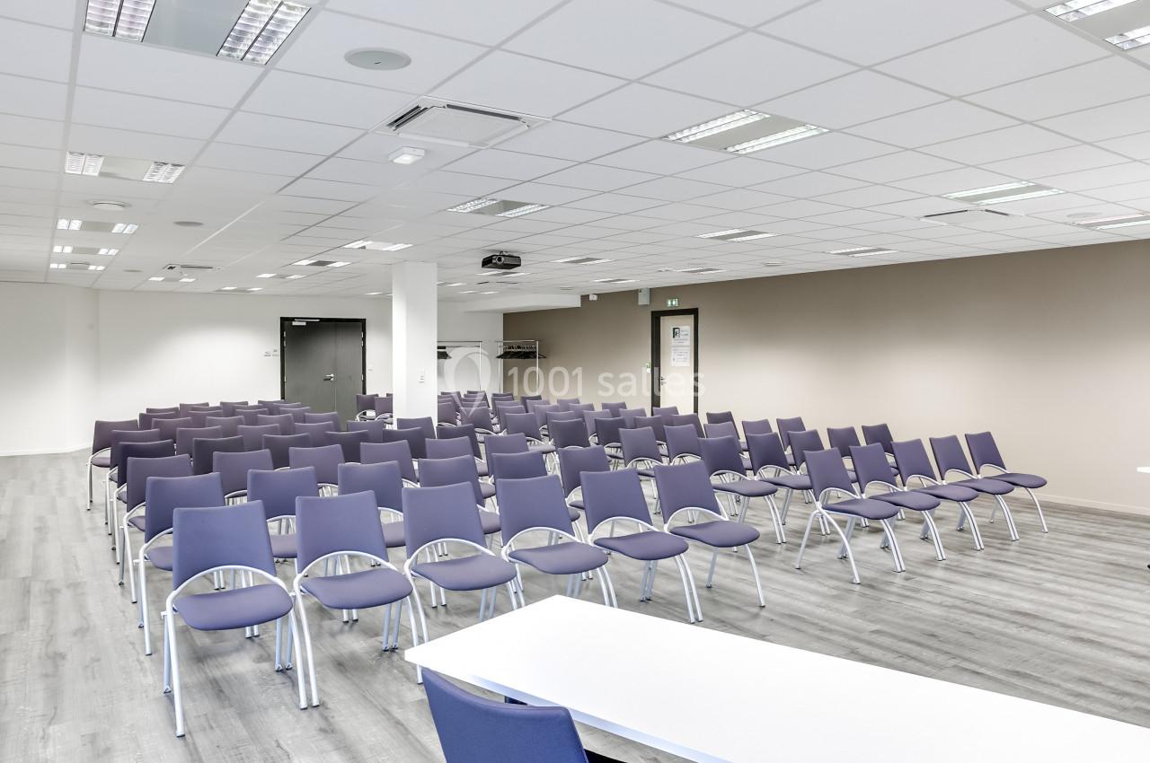 Salle de conférence lumineuse avec des rangées de chaises violettes alignées face à une table blanche.