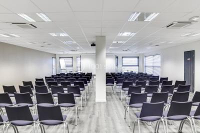 Façade moderne d'un bâtiment nommé ’Hôtel d'Entreprises Colisée’, entouré de verdure sous un ciel bleu.