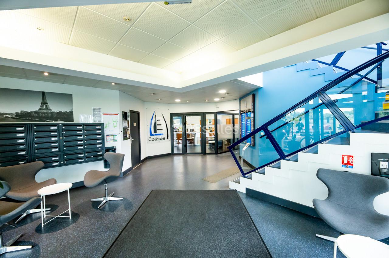 Hall d'entrée moderne avec sièges, boîtes aux lettres, escalier bleu et porte vitrée menant à des bureaux.