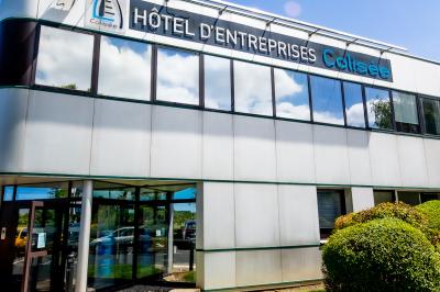 Façade moderne d'un bâtiment nommé ’Hôtel d'Entreprises Colisée’, entouré de verdure sous un ciel bleu.