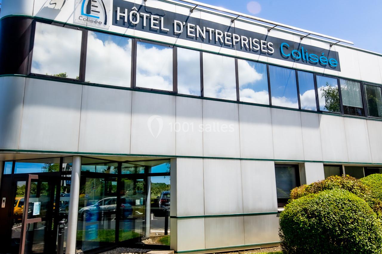 Façade moderne d'un bâtiment nommé ’Hôtel d'Entreprises Colisée’, entouré de verdure sous un ciel bleu.