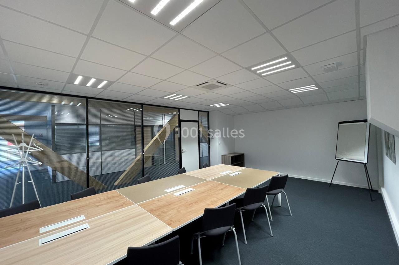 Salle de réunion moderne avec grande table en bois, chaises noires, tableau blanc et cloisons vitrées.